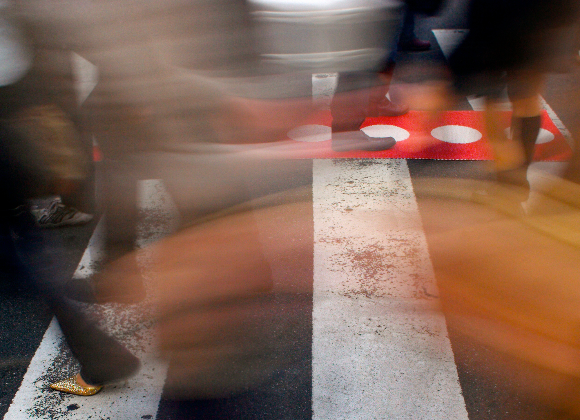 Vera Teppich von Pappelina: Menschen überqueren Zebrastreifen mit rotem Teppich mit weißen Punkten.