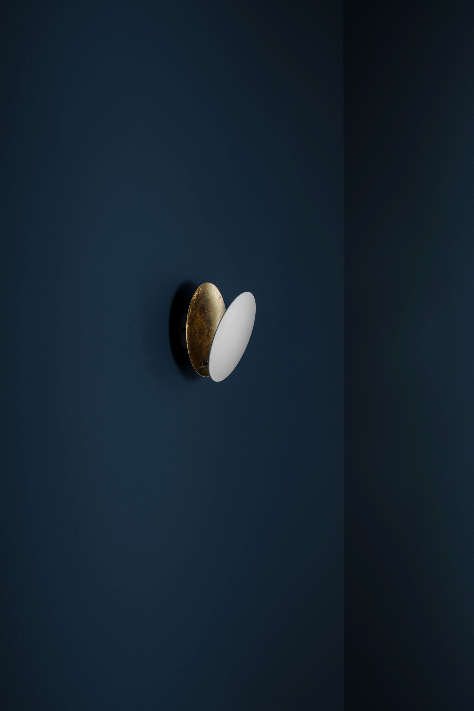 Lederam Wandleuchte von Catellani & Smith in Gold und Weiß an blauer Wand.