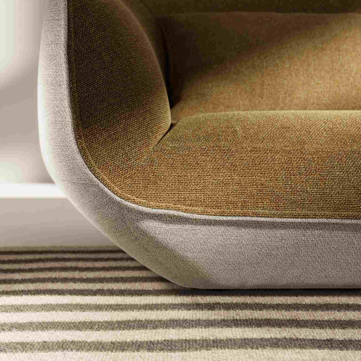 Detailaufnahme des Nook Sofas mit braunem Sitz und grauem Rahmen auf gestreiftem Teppich.