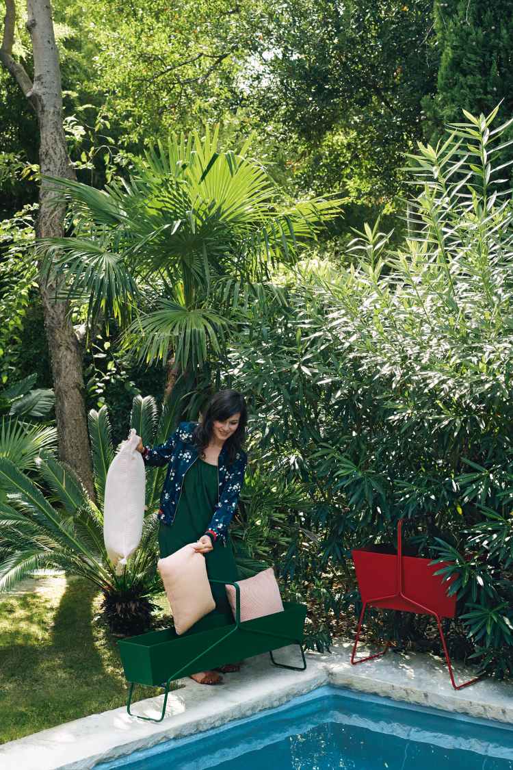 Frau befüllt grünen Fermob Basket Blumenkasten lang im Garten mit Kissen. Metall Blumenkästen.