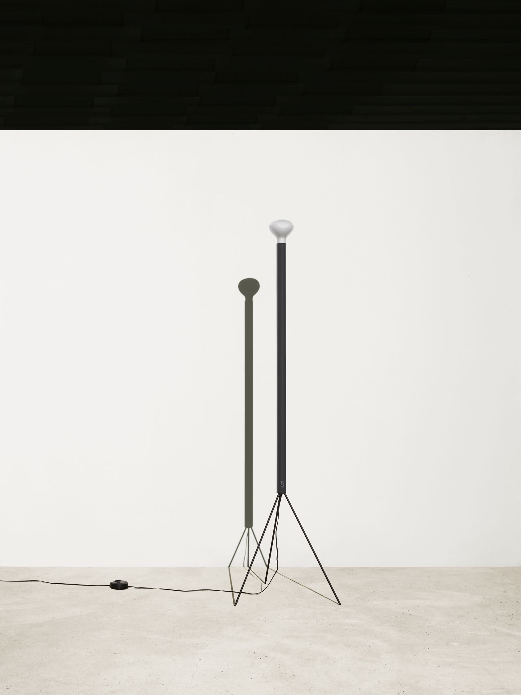 Weisse Flos Luminator Stehleuchte mit schwarzem Metallfuß und hellem Leuchtkopf für modernes Wohnambiente.