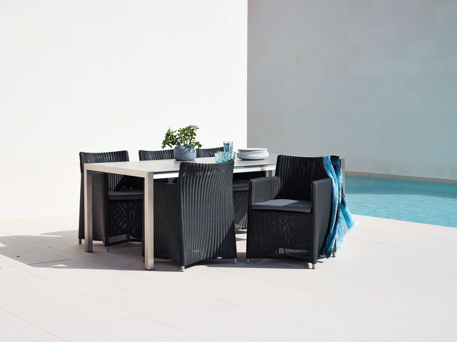 Cane-Line Diamond Outdoor Stuhl aus schwarzem Rattan mit Armlehnen an Esstisch am Pool.