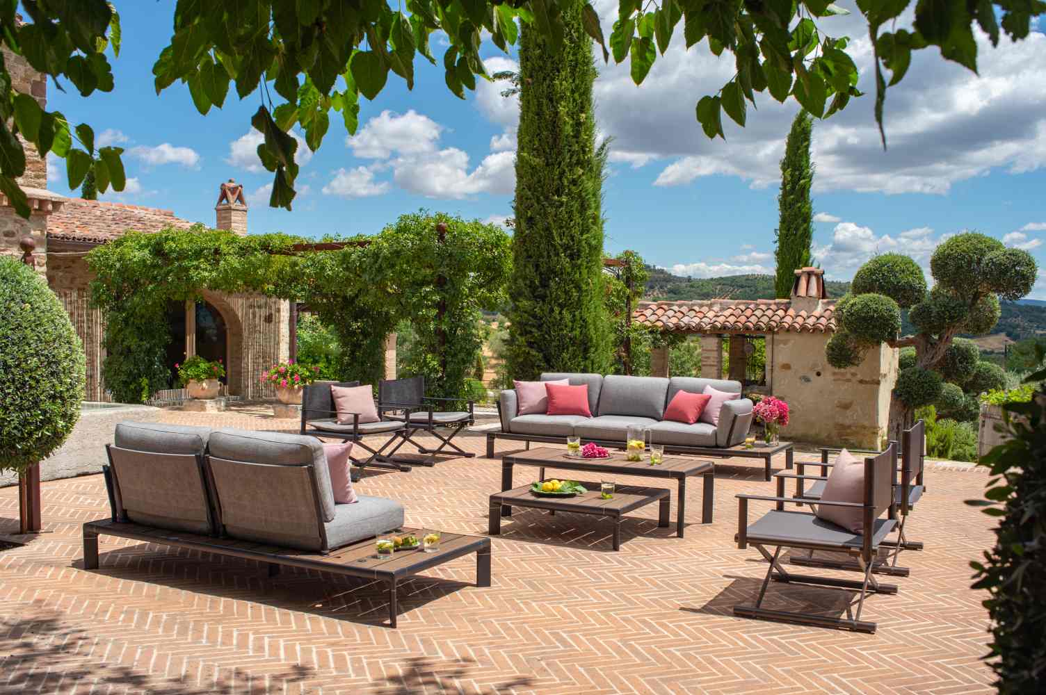 Emu Terra Fußhocker Outdoor-Möbel auf einer sonnigen Terrasse mit Lounge-Sofa und Sesseln.