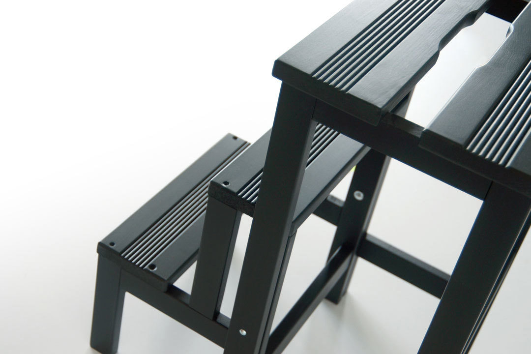Nahaufnahme einer schwarzen Hockerleiter aus Holz mit zwei Stufen.