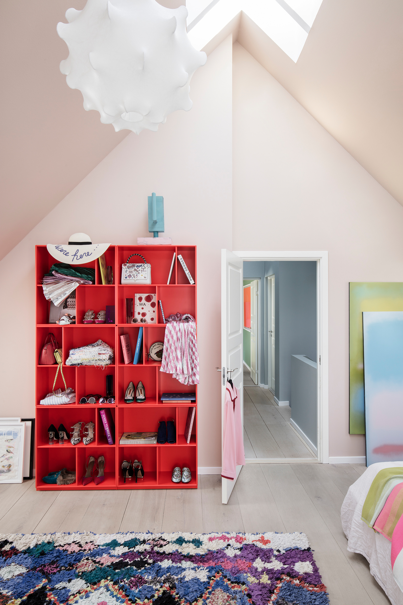 Rotes Montana Bücherregal im Dachgeschoss, gefüllt mit Büchern, Schuhen und Accessoires. Modernes Regaldesign.