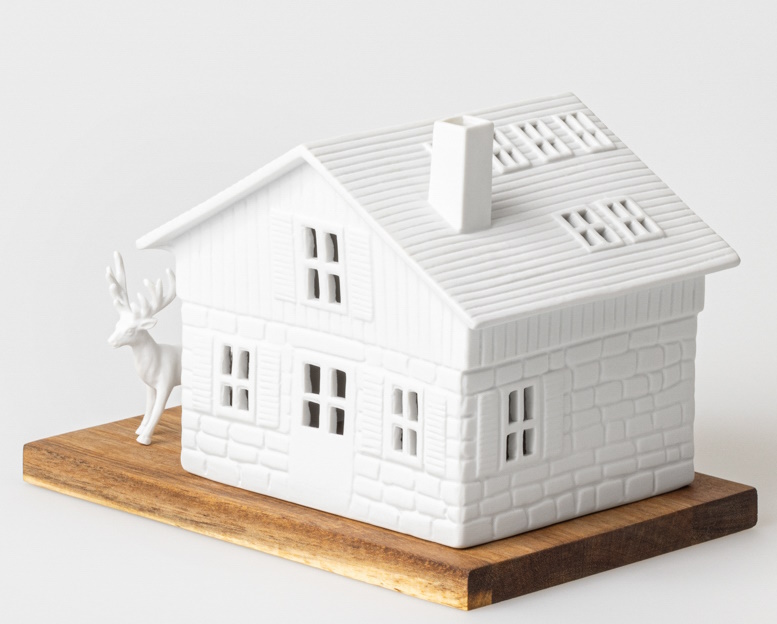 Lichthaus Skihütte Räder: Weißes Porzellanhaus mit Hirschfigur auf Holzsockel, stimmungsvolle Winterdekoration.