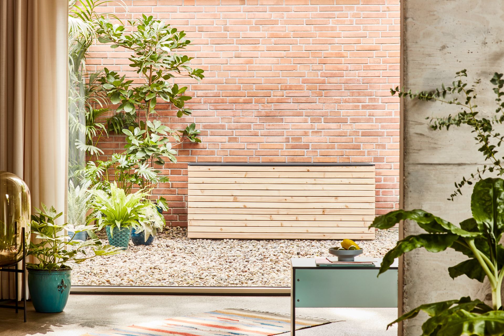 Forte Kissentruhe aus Lärche und Anthrazit vor einer Backsteinmauer im Außenbereich.