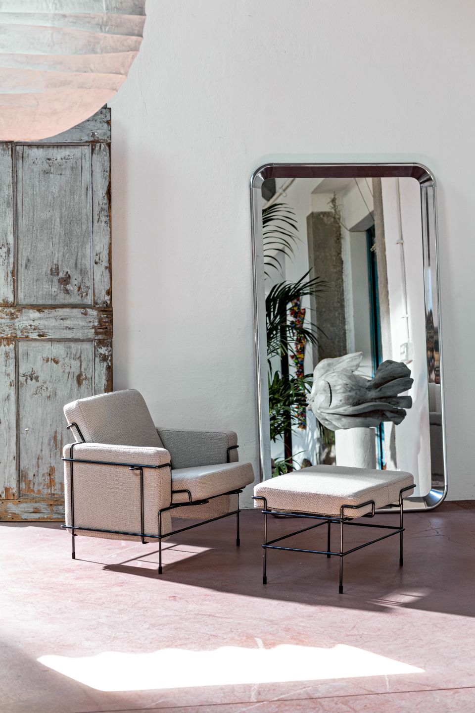 Freistehender Deja-vu Spiegel von Magis, reflektiert einen Sessel und Hocker in einem hellen Raum.