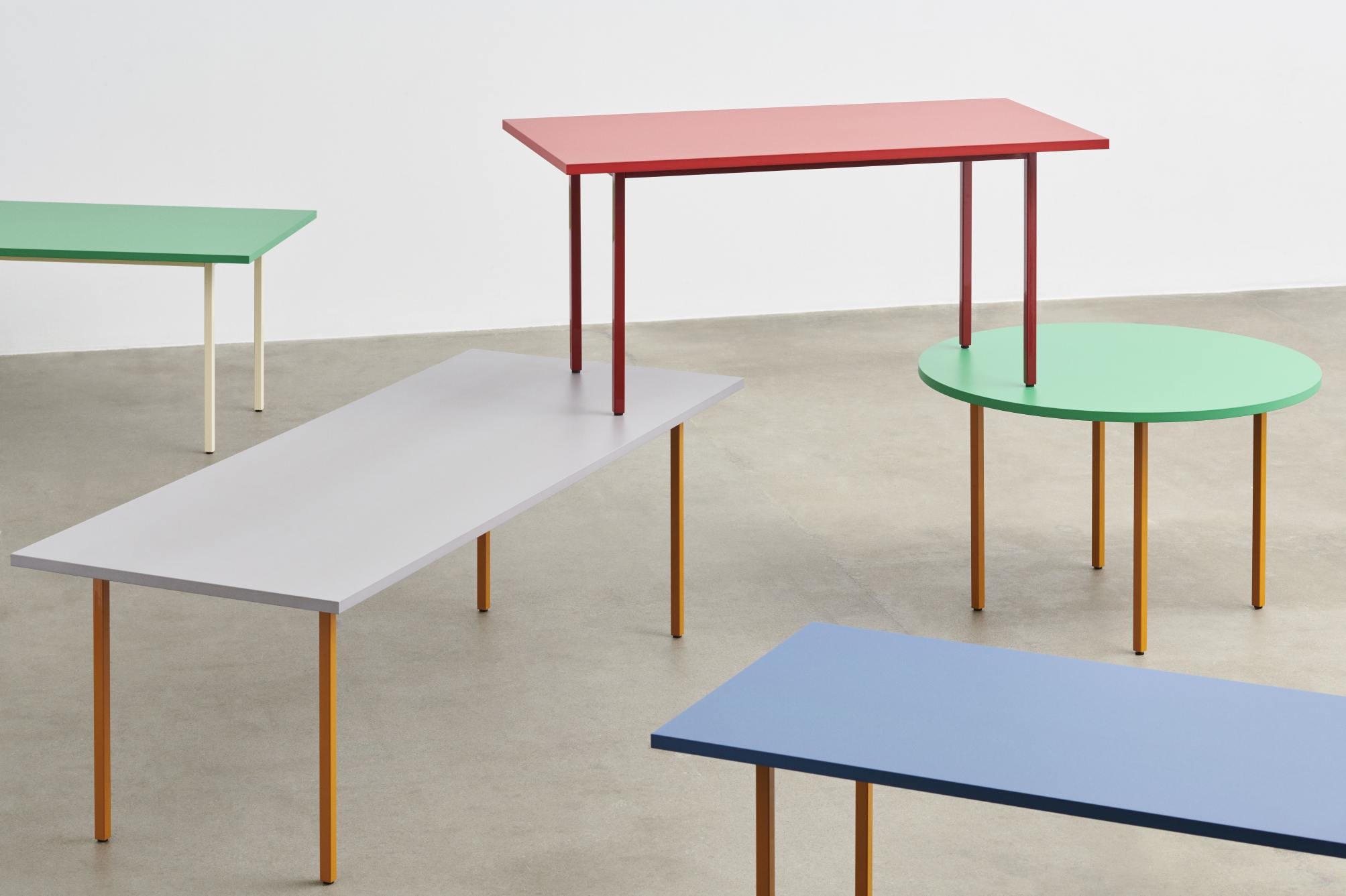 Mehrere farbige Tische der Two Colour Table Serie von Hay in verschiedenen Formen und Größen.