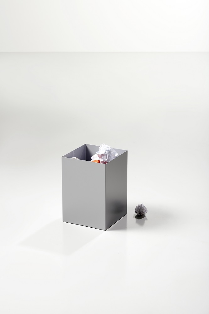 Grauer, quadratischer Cascando Papierkorb mit Papierknäueln, Büromüll und einem zerknüllten Papierball daneben.