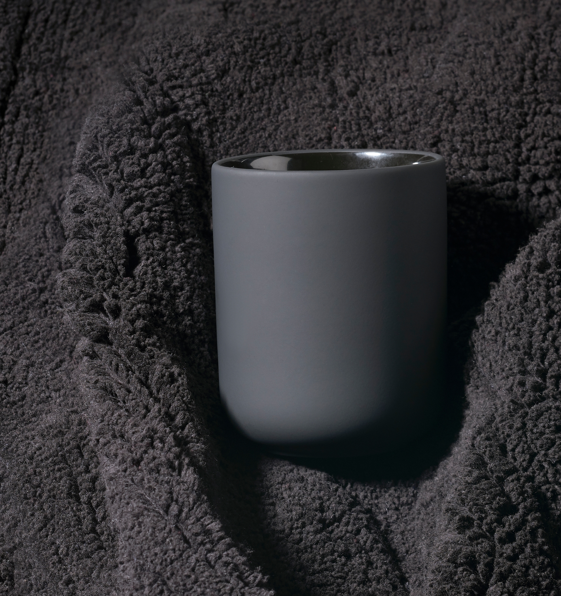 Grauer Ume Zahnputzbecher von Zone Denmark auf dunklem, strukturiertem Stoff für Badezimmeraccessoires und moderne Badgestaltung.