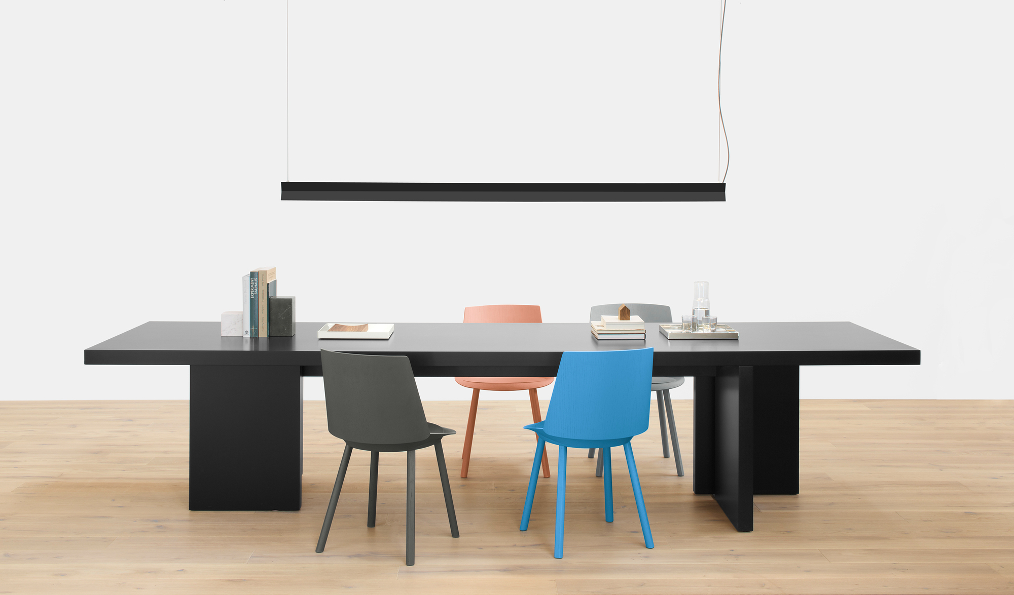 Schwarzer Esstisch mit farbigen Stühlen und einer schwarzen Hängeleuchte. Bücher stehen mit e15 AC11 Stop Buchstützen auf dem Tisch.