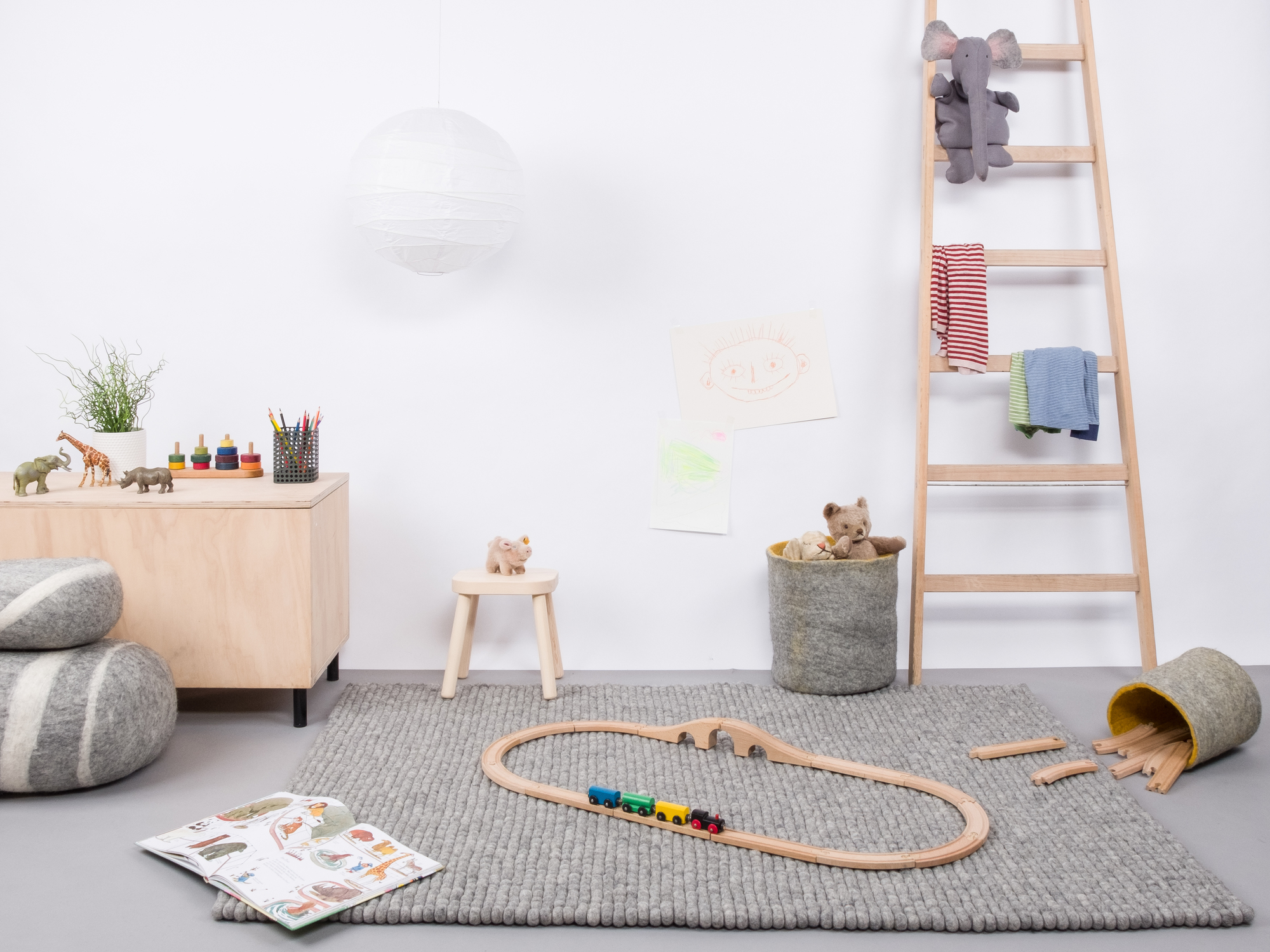 Grauer Filzkugel Teppich 160x230 cm im Kinderzimmer mit Spielzeug und Holzeisenbahn.