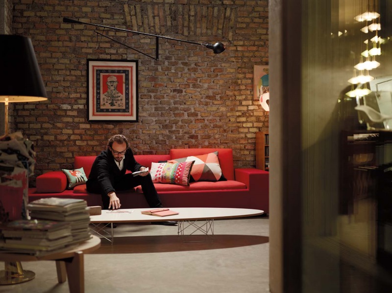 Wohnzimmer mit Gueridon Tisch von Vitra, rotem Sofa und Person. Designermöbel für stilvolles Wohnen.