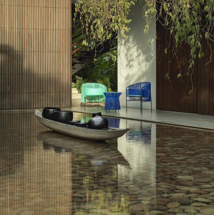 Caribe Dining Chair Outdoor: Türkis- und smaragdgrüne Gartenstühle neben einem Wasserbecken mit Steinen.