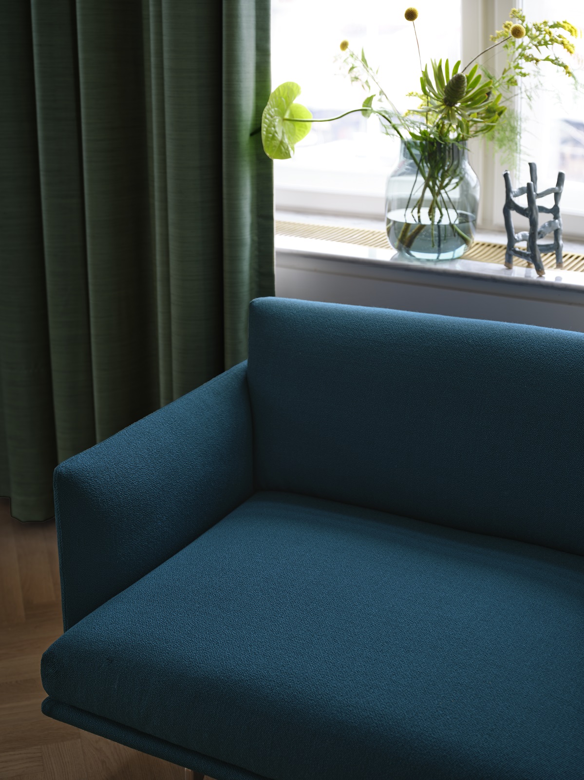 Nahaufnahme des Muuto Outline Studio Sofas in Türkis, vor einem Fenster mit Vorhängen.