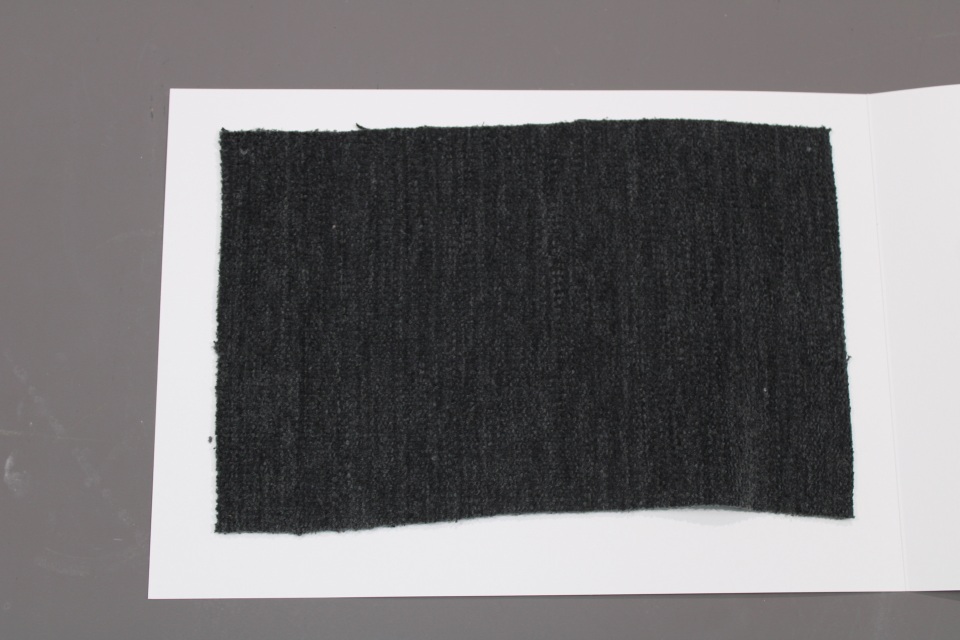 Stoffmusterkarte Gruppe 81 Cor: Nahaufnahme eines dunkelgrauen, gewebten Stoffmusters auf weißem Karton.