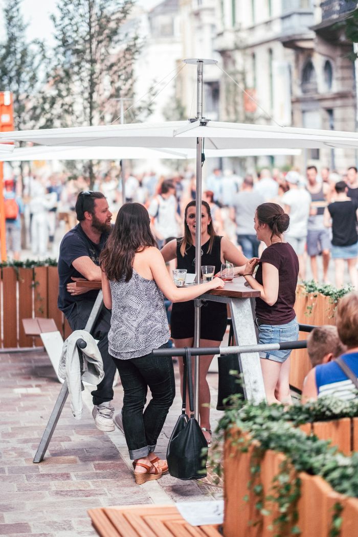 Gruppe von Personen unter einem weißen Inumbrina Sonnenschirm im Freien. Sonnenschutz und Design.