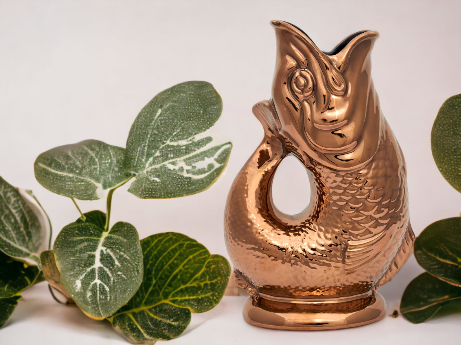 Kupferfarbene Gluckigluck Fischkaraffe mit Pflanzen auf weißem Hintergrund, dekorative Wasserkaraffe für Tisch und Küche.