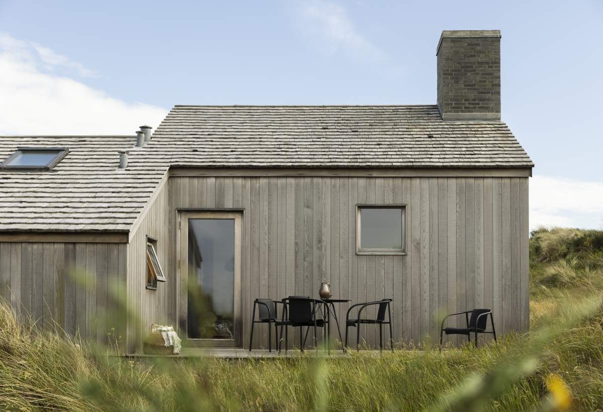 Houe Nami Lounge Chair Sessel Outdoor vor Holzhaus mit Tisch und Stühlen im Garten.