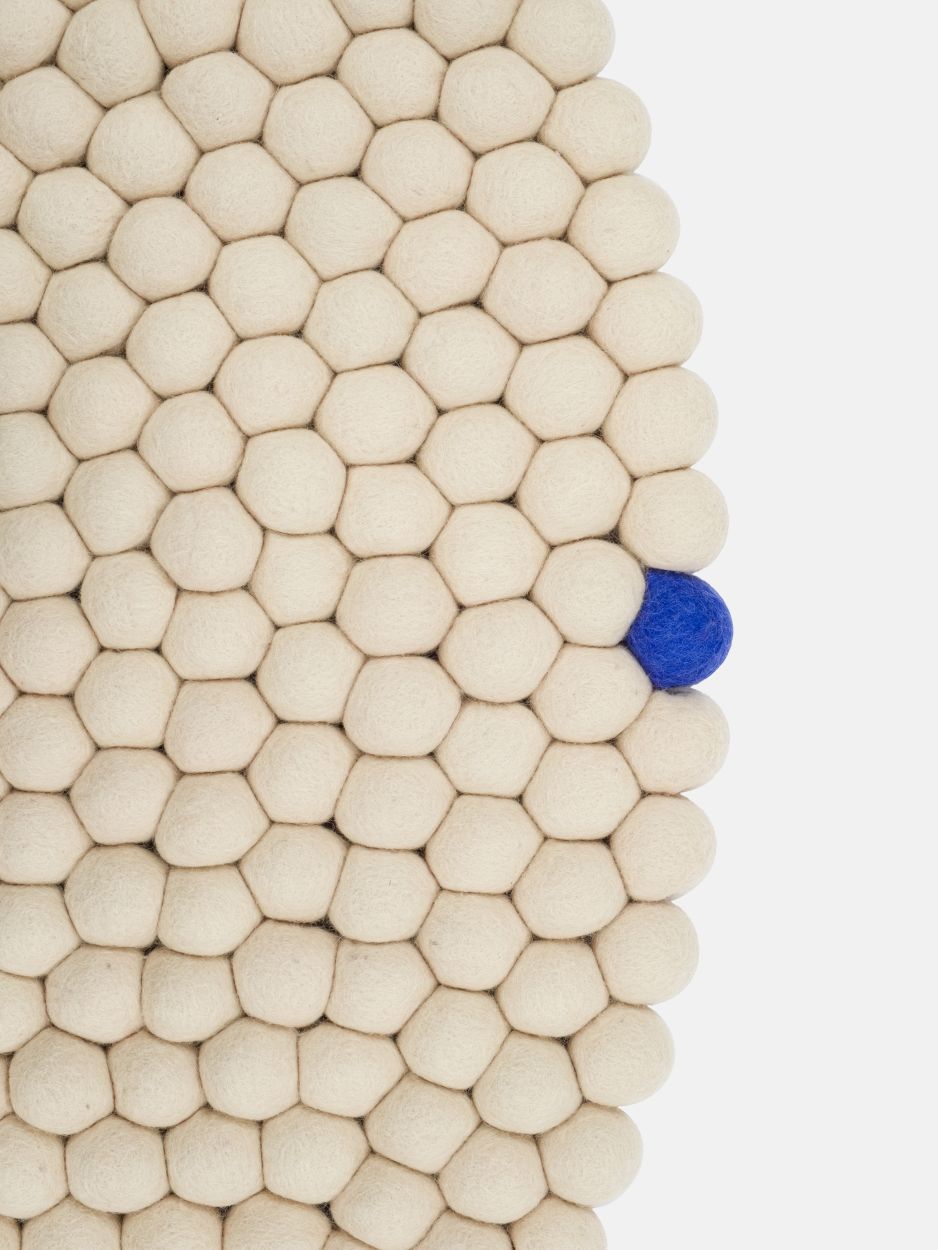 Detailaufnahme des beigen myfelt Filzteppichs mit runden Filzkugeln und einer blauen Kugel.