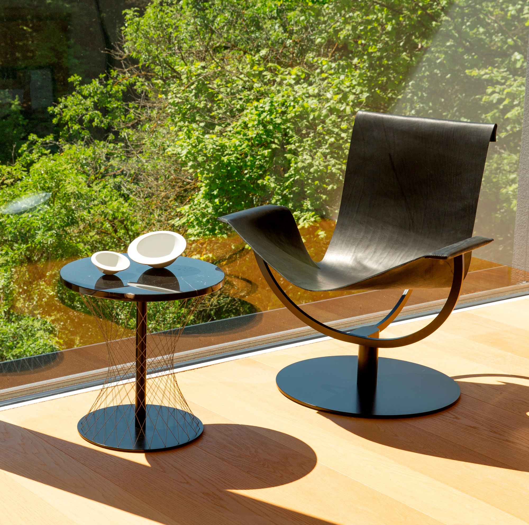 Zwei weiße Pivot Schalen 20 cm auf einem schwarzen Beistelltisch neben einem Design-Sessel.