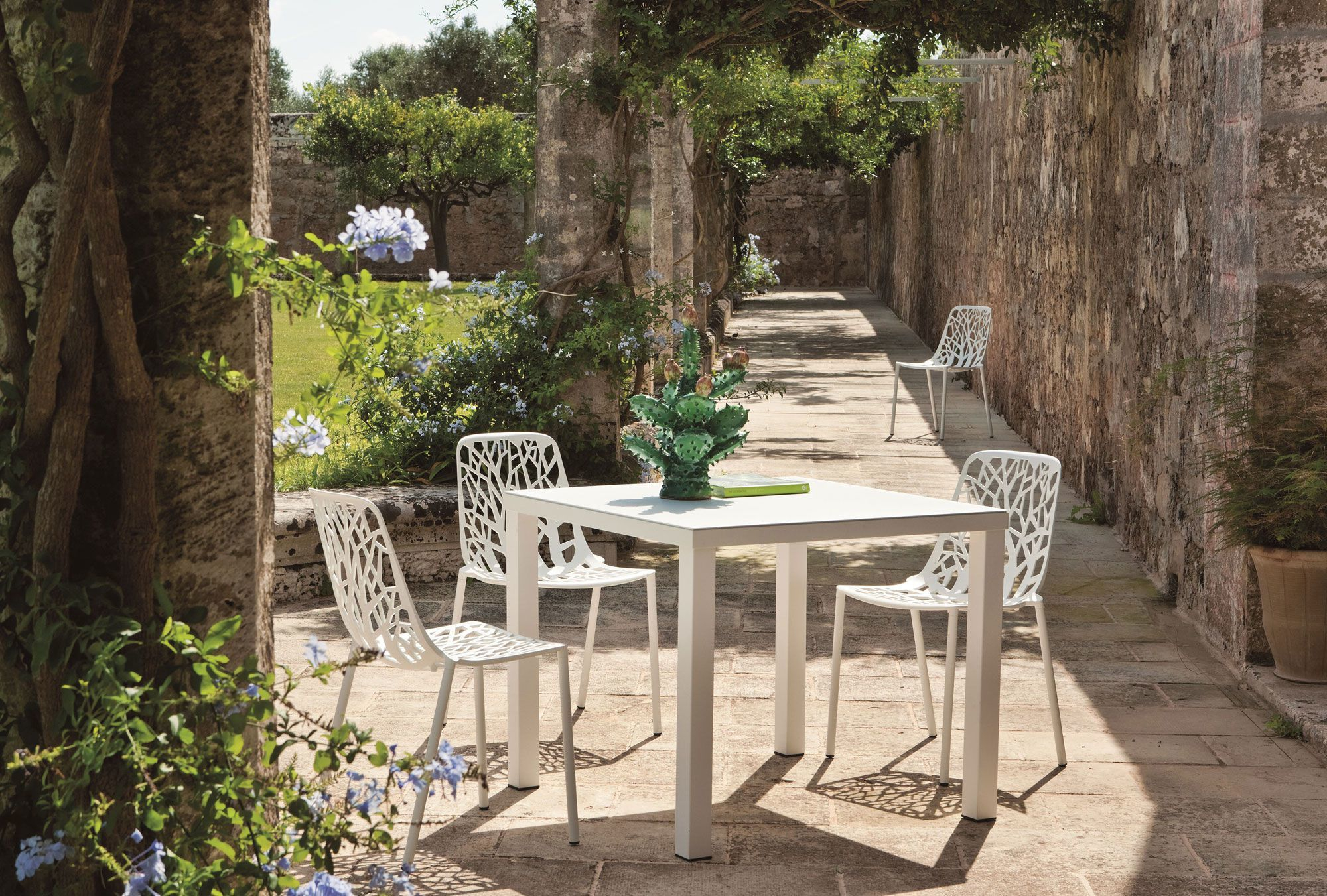 Weißer Forest Outdoor Stuhl mit filigranem Design am Gartentisch im Freien. Gartenmöbel für Terrasse.