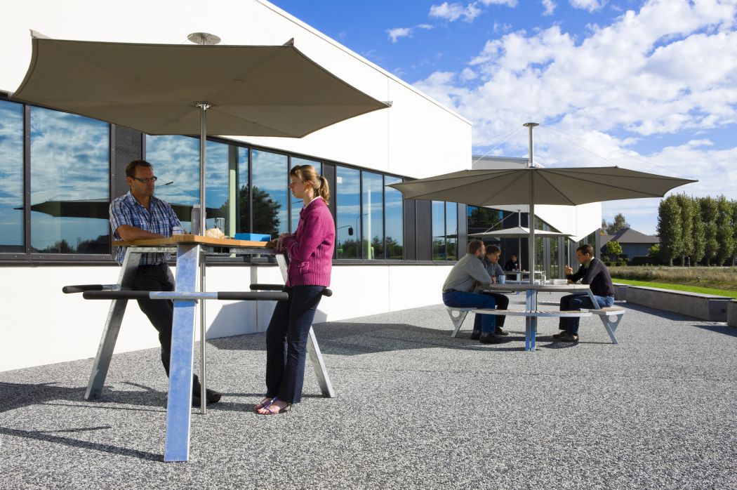 Inumbrina Sonnenschirm von Extremis spendet Schatten über einer Gruppe von Menschen im Freien.