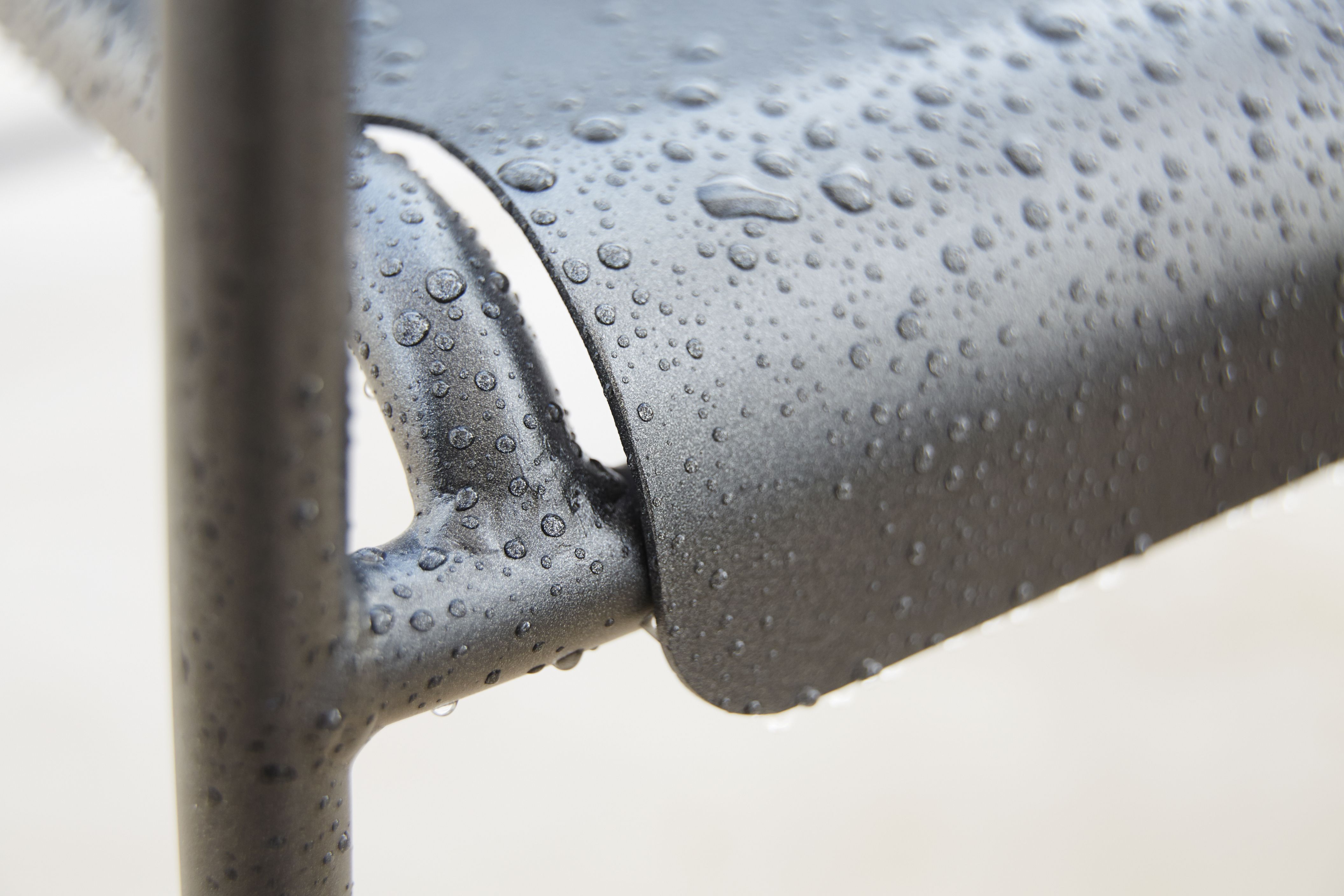 Detailaufnahme: Cane-Line Copenhagen Armlehnstuhl, schwarzes Metall mit Wassertropfen, wetterfester Outdoor Stuhl.