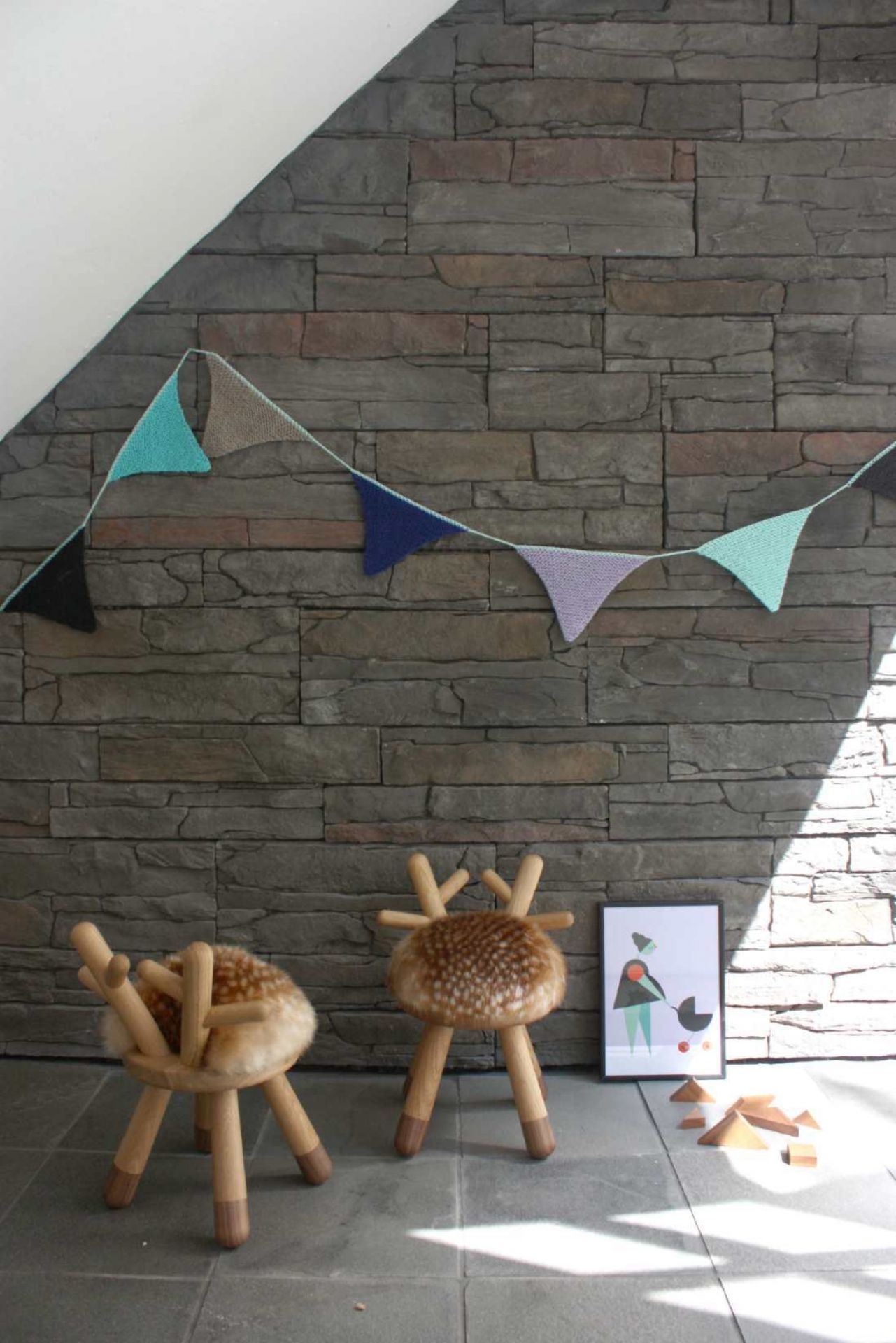 Zwei Kinderhocker im Hirschdesign mit Fellimitat vor Steinwand mit bunter Wimpelkette.