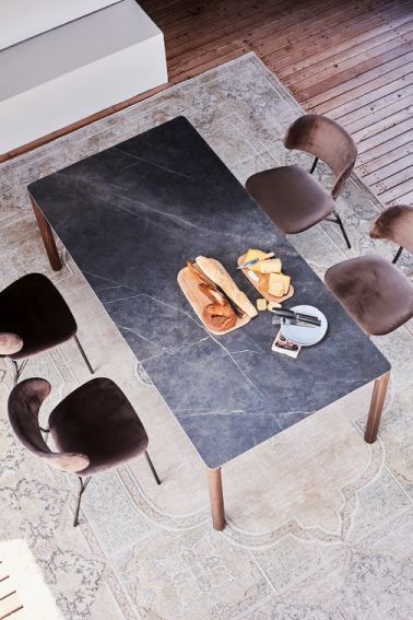 Radius Tisch von Jan Kurtz mit dunkler Marmorplatte und vier Stühlen, gedeckt mit Brot und Käse.