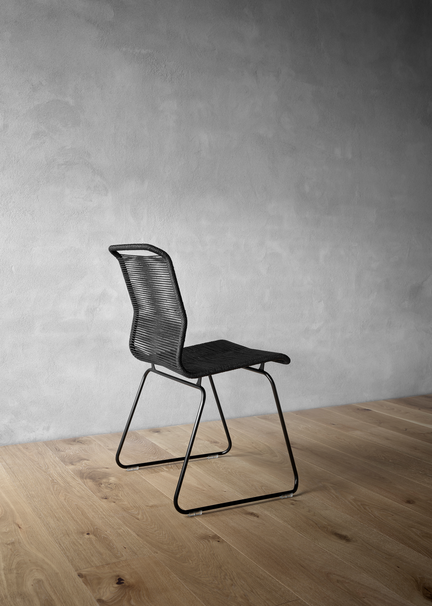 Schwarzer Panton One Stuhl mit Kordelbespannung und schwarzem Metallgestell auf hellem Holzboden. Design Stuhl.