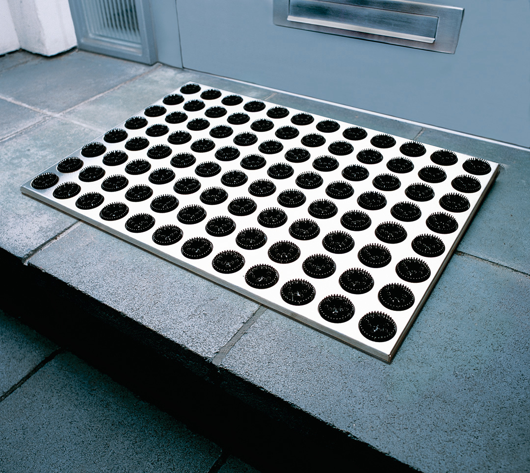 Feet-Back Fußmatte mit Noppen: Weiße Fußmatte mit schwarzen Noppen vor einer Haustür.