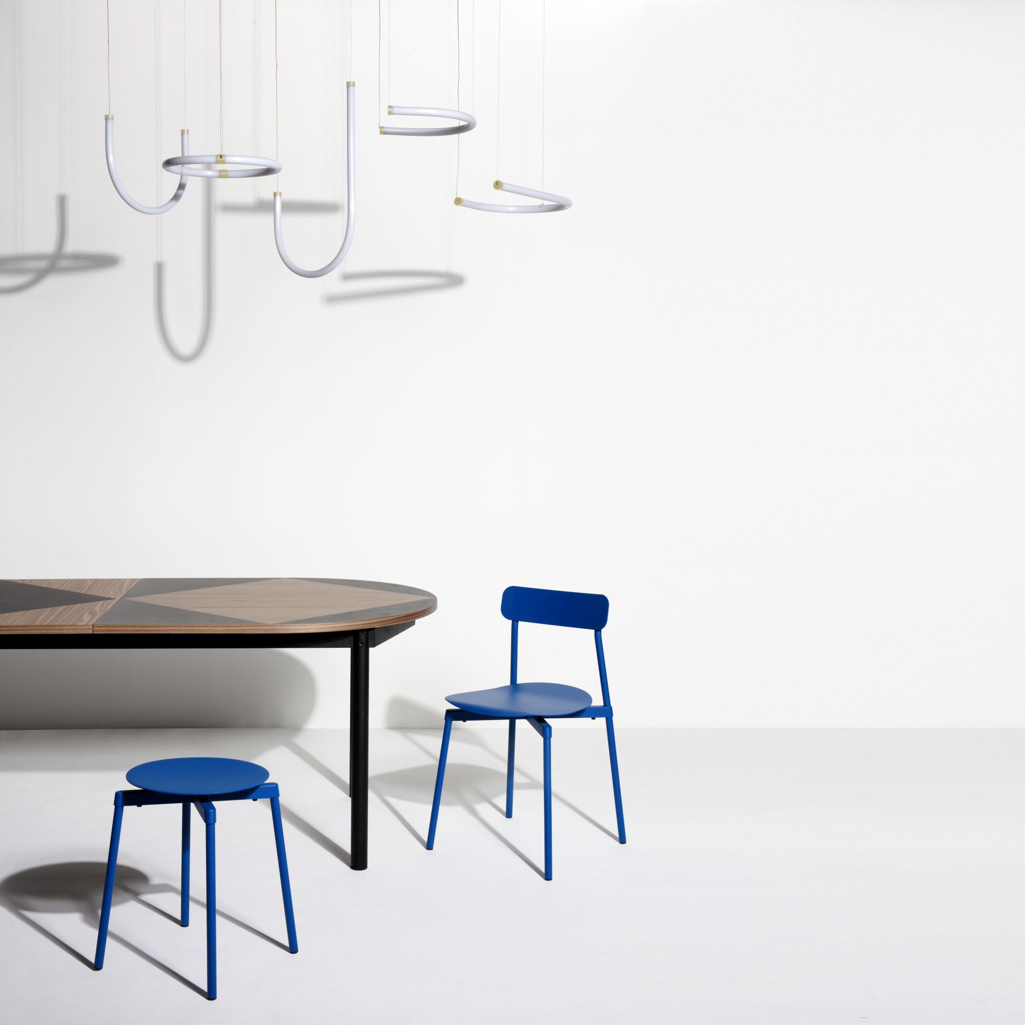 Blauer Fromme Stool Hocker von Petite Friture neben einem Tisch und Stuhl in minimalistischem Interieur.