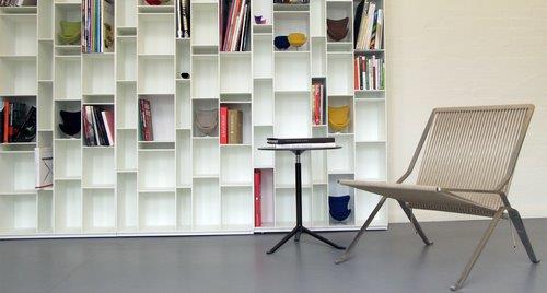 Beiger PK25 Sessel von Fritz Hansen mit minimalistischem Design und Stahlgestell vor Bücherregal.