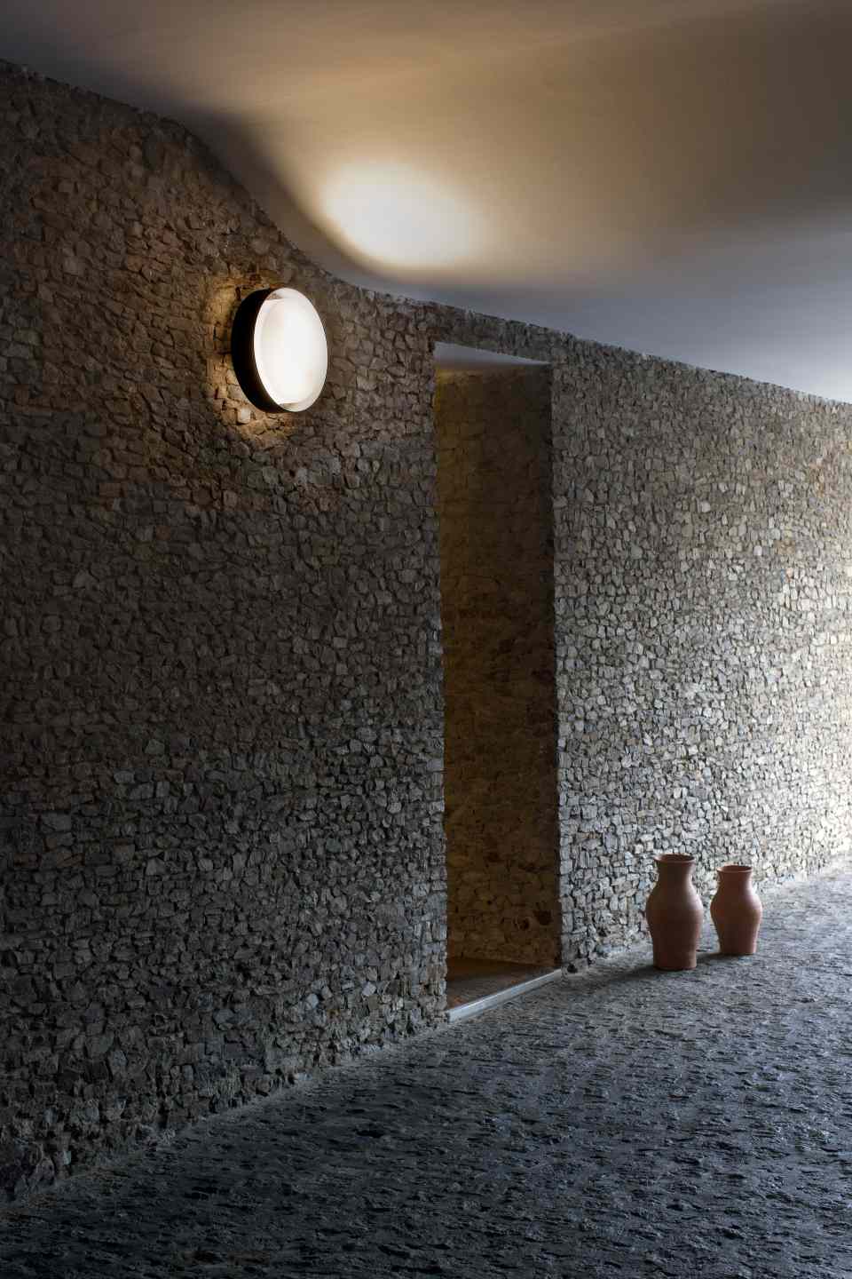 Plaff-On! Wandleuchte in Rostbraun an Steinwand, runde Außenleuchte für stimmungsvolle Beleuchtung.