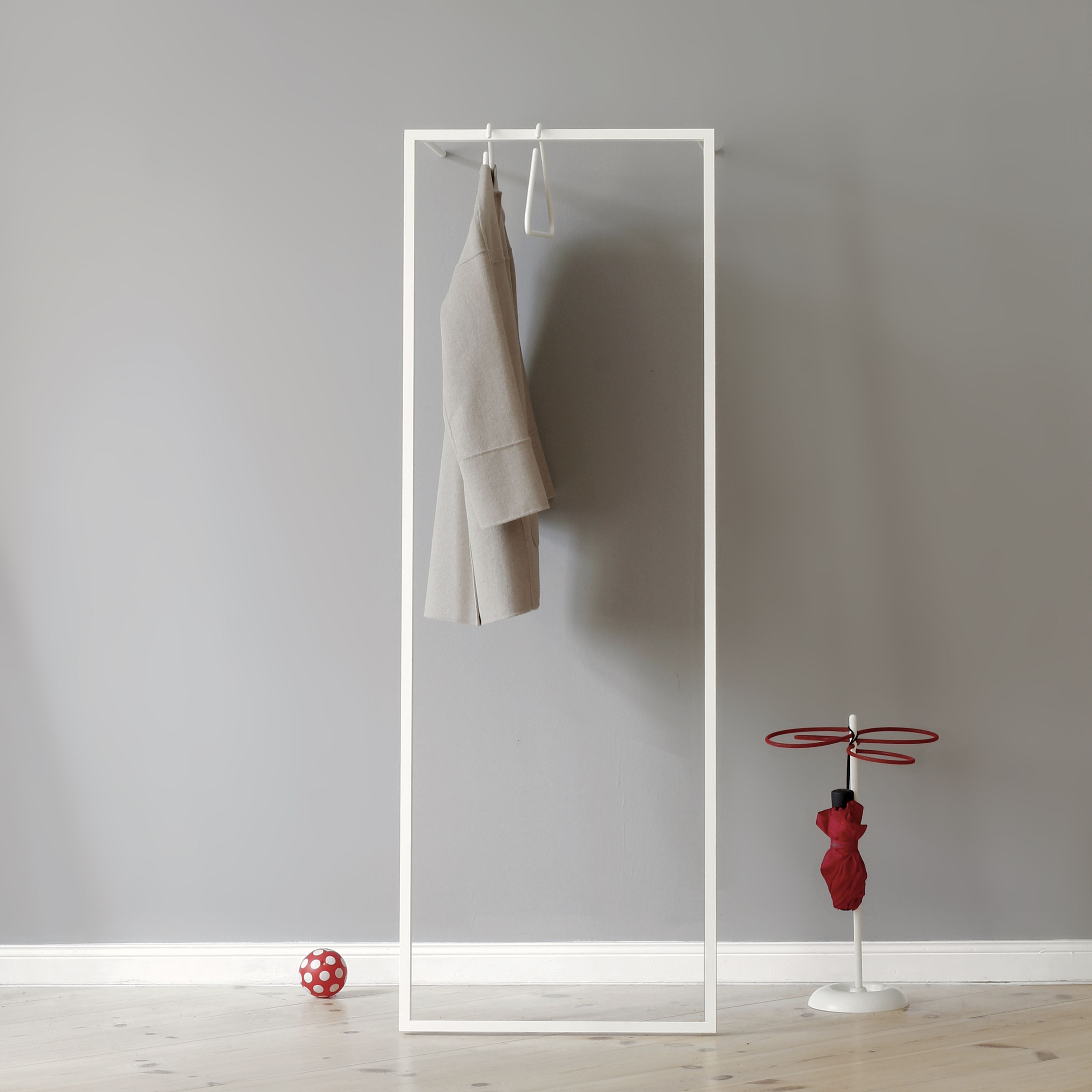 Weiße Leano S Anlehngarderobe von Roomsafari mit Mantel, Schirmständer und Ball vor grauer Wand.