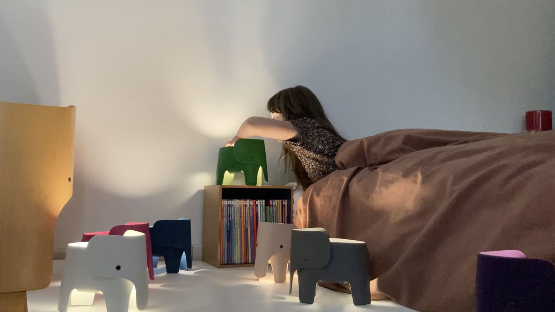 Mädchen schaltet grüne Elefantenlampe ein, umgeben von bunten Elefantenhockern im Kinderzimmer.