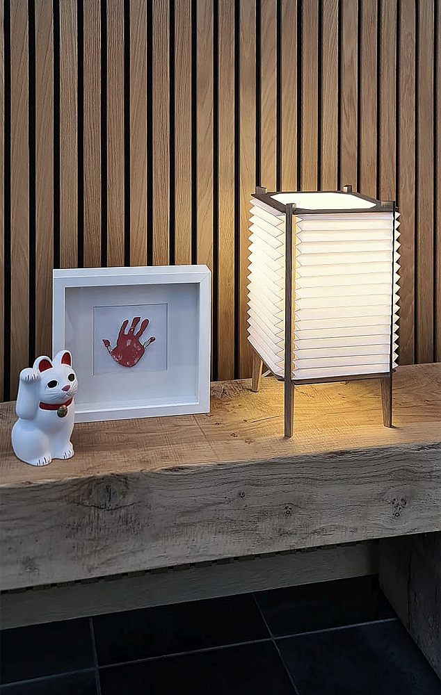 BEE HIVE Tischleuchte von Le Klint: Quadratische Designerlampe mit plissiertem Lampenschirm auf einem Holztisch.