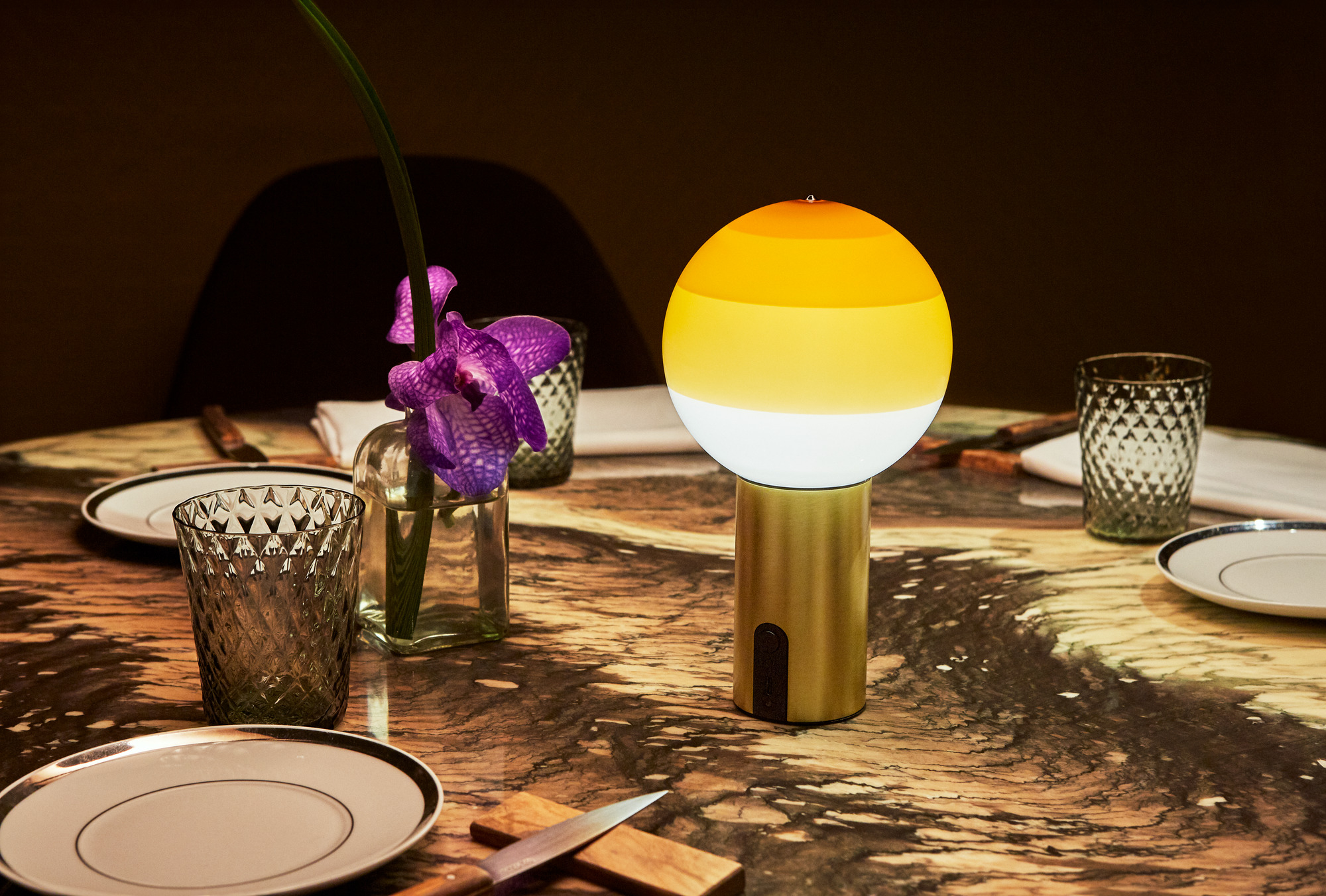 Marset Dipping Light Portable LED Akkuleuchte auf gedecktem Tisch mit Geschirr und Blumenvase.