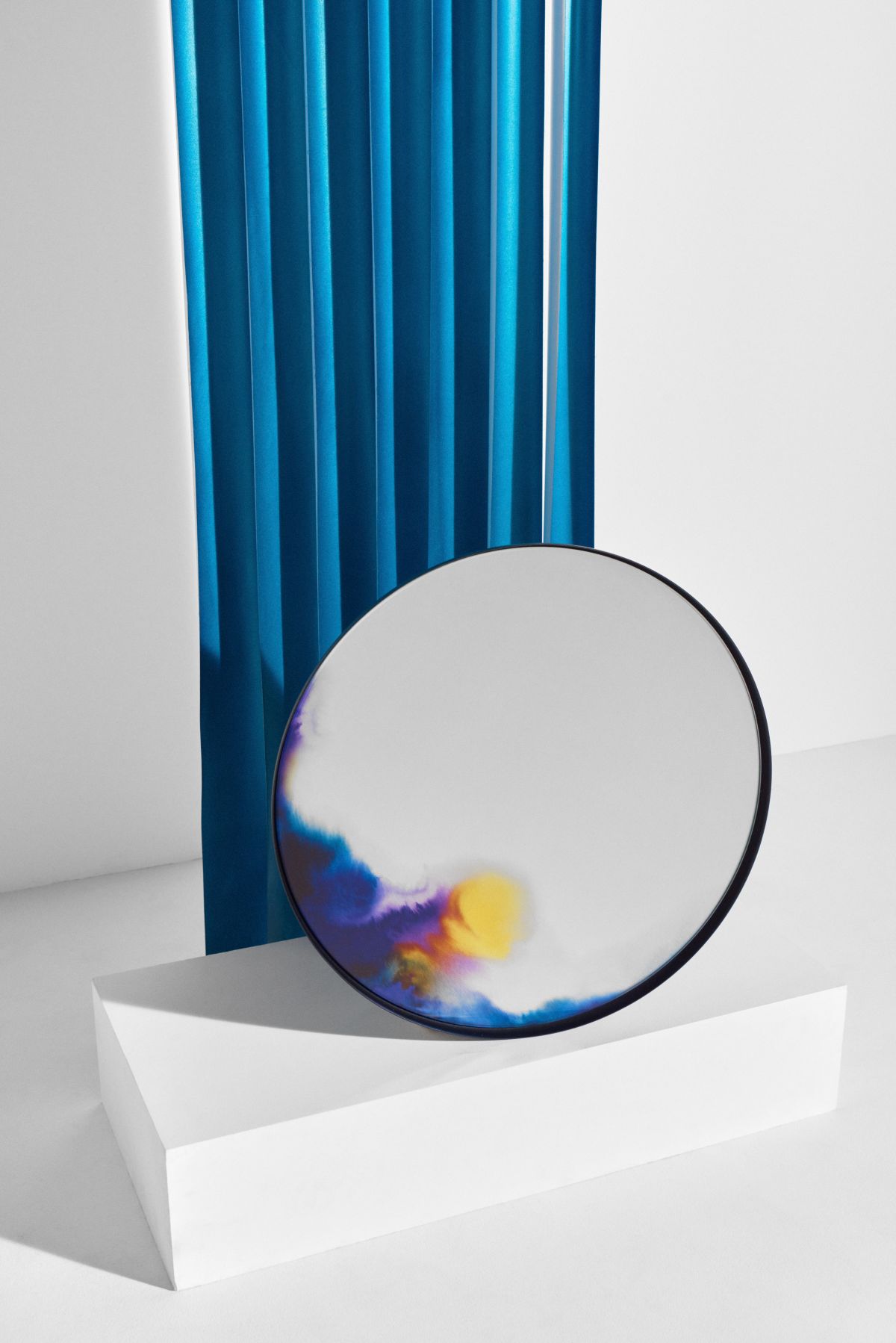 Runder Wandspiegel mit abstraktem Farbverlauf in Blau, Gelb und Lila auf weißem Hintergrund.