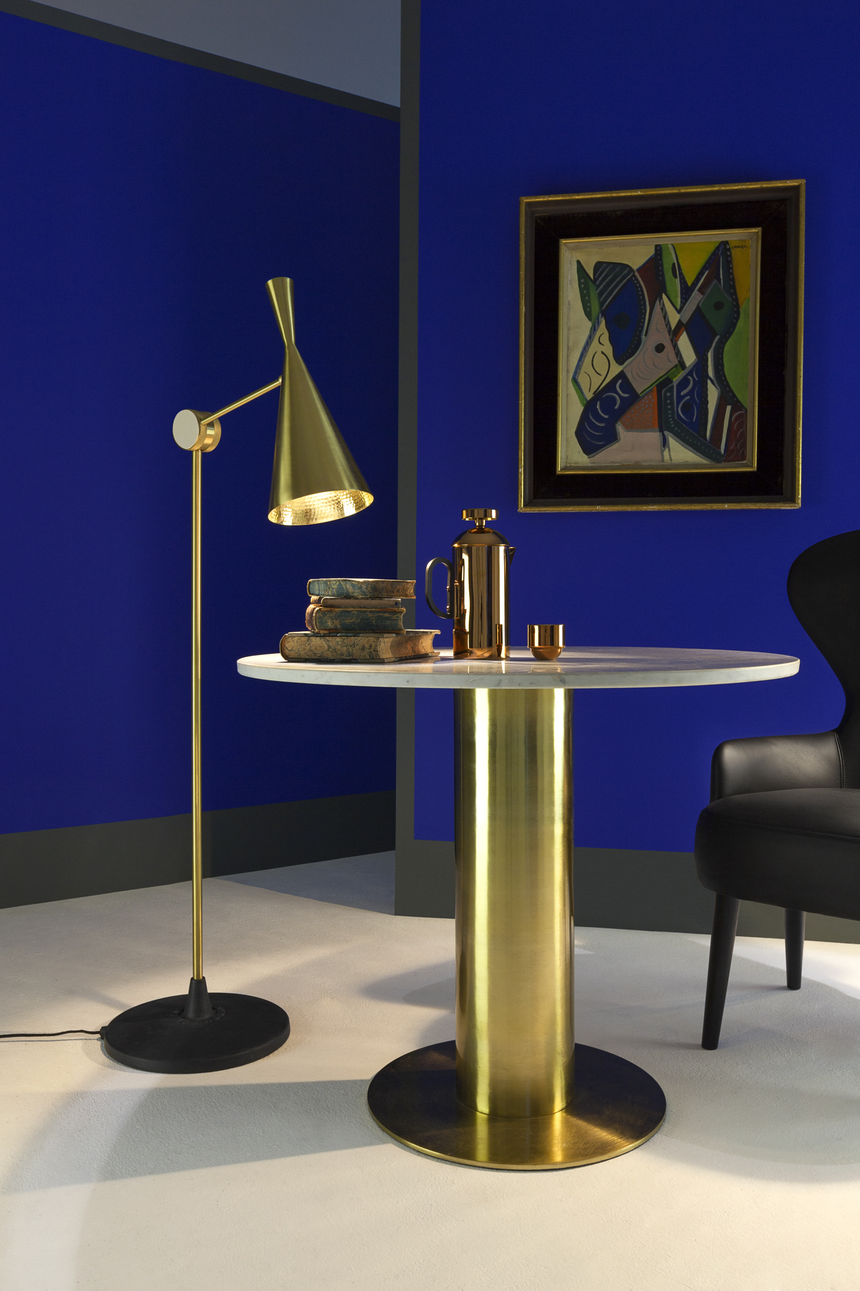 Goldene Beat Stehleuchte von Tom Dixon neben rundem Tisch mit Deko vor blauer Wand.
