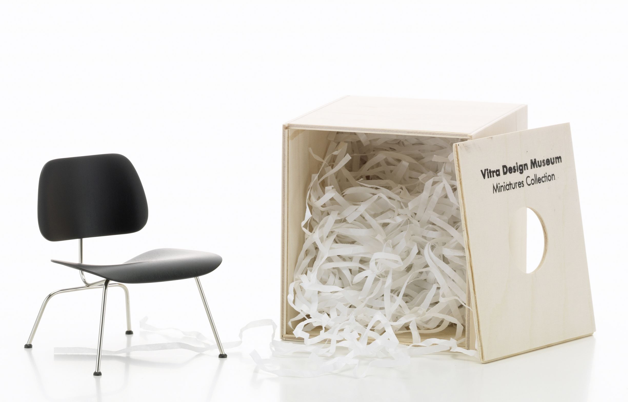 LCM Miniatur Stuhl von Vitra neben einer offenen Holzkiste mit Papierstreifen.