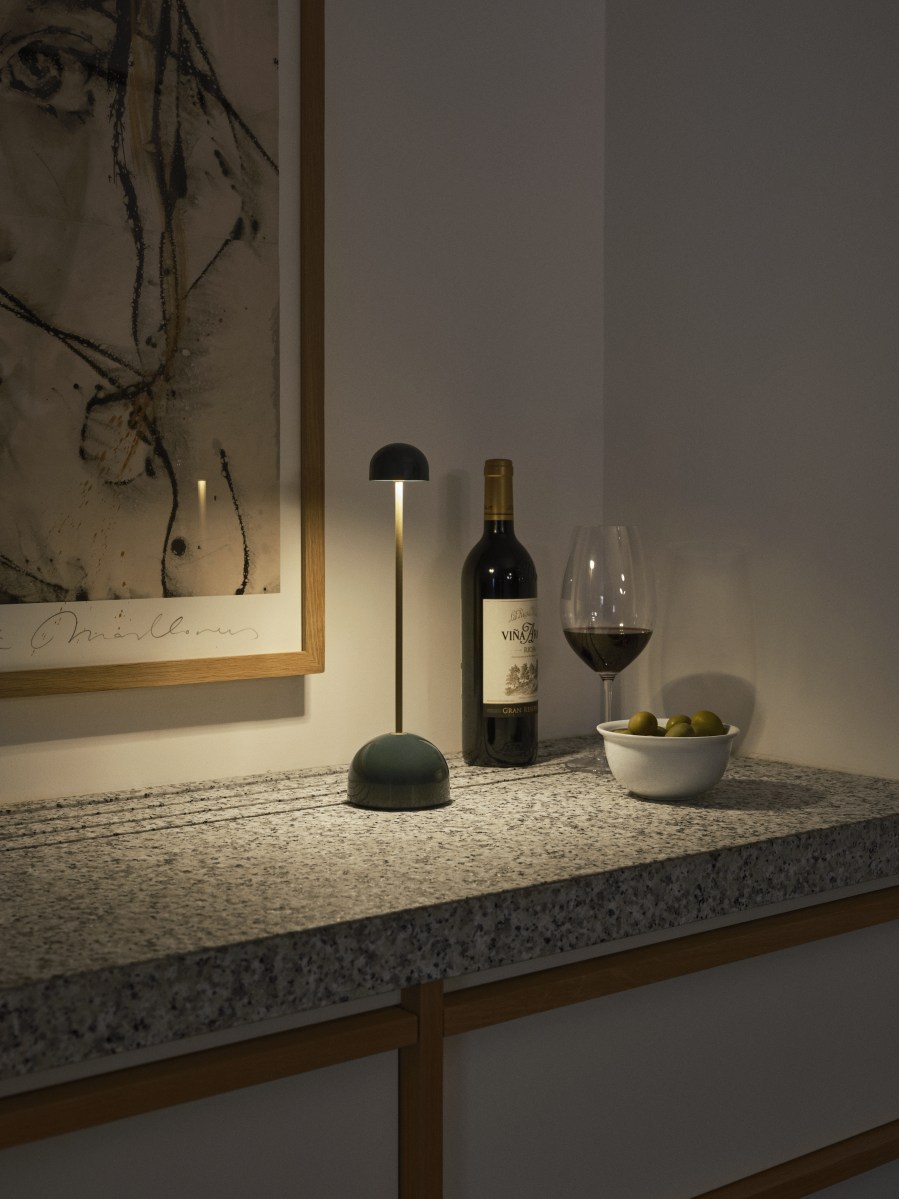 Sips Akkuleuchte von Marset, weiße Tischleuchte mit silbernem Ständer neben Wein und Oliven.