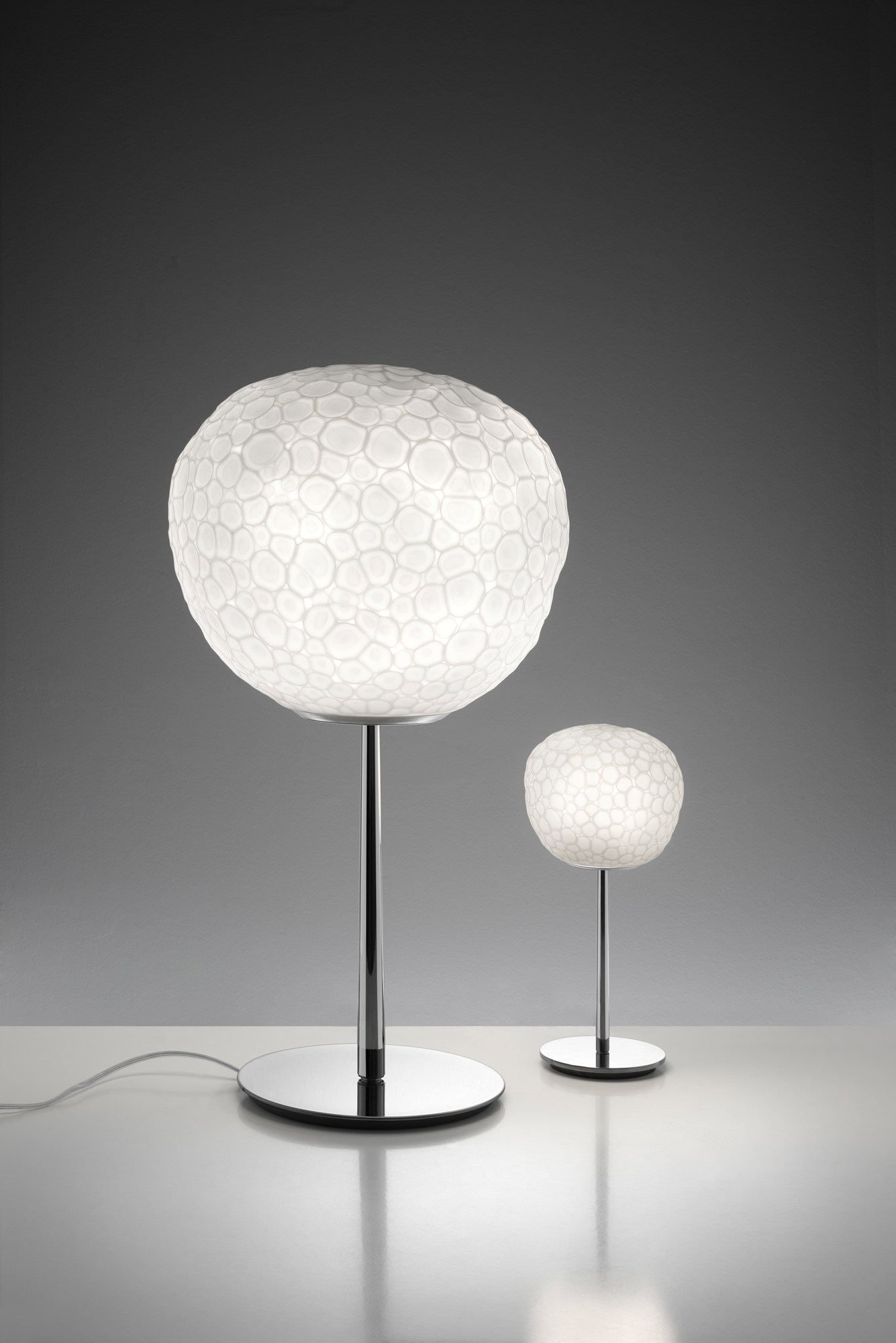 Meteorite Tischleuchte von Artemide: Zwei moderne Lampen mit kugelförmigem, strukturiertem Glas und Chromfuß.