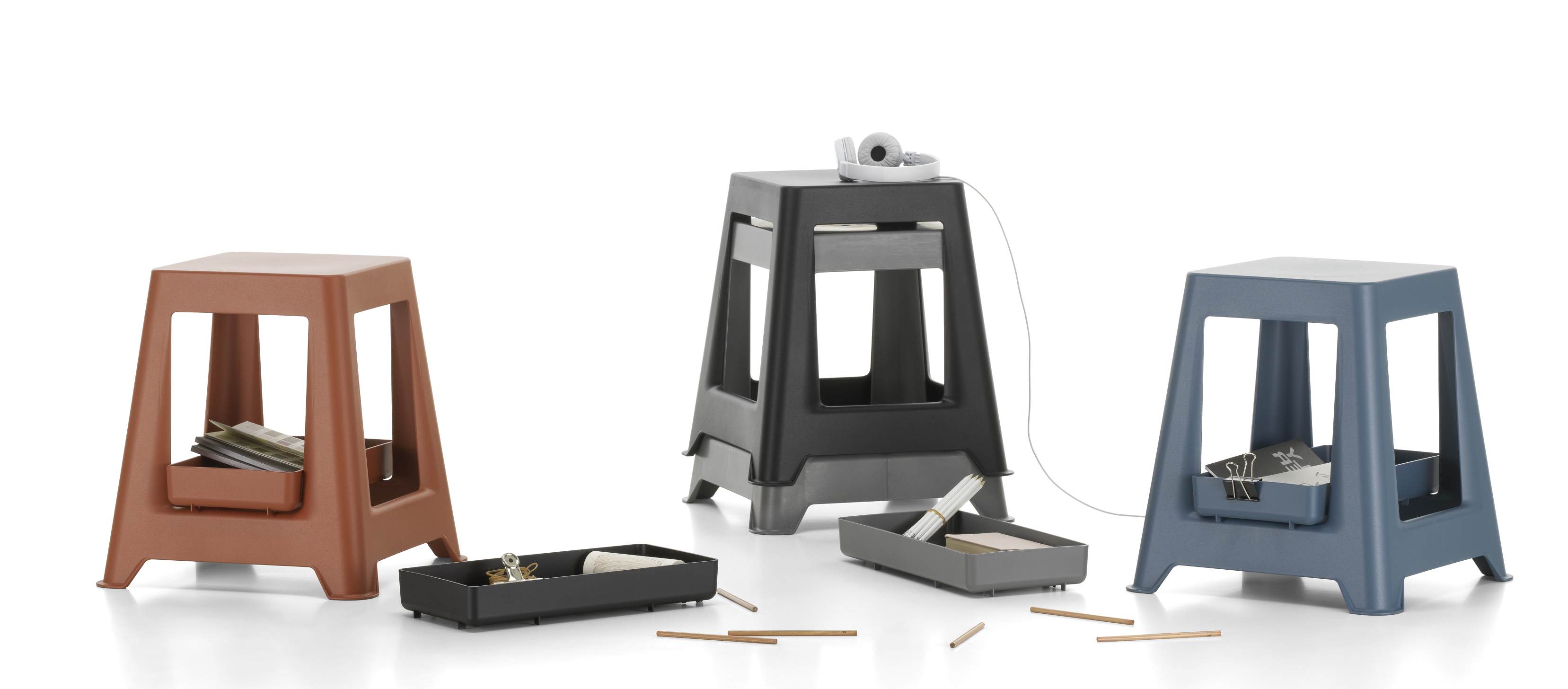 Drei Chap Tray Hocker von Vitra in Braun, Dunkelgrau und Blau mit Ablagefächern.