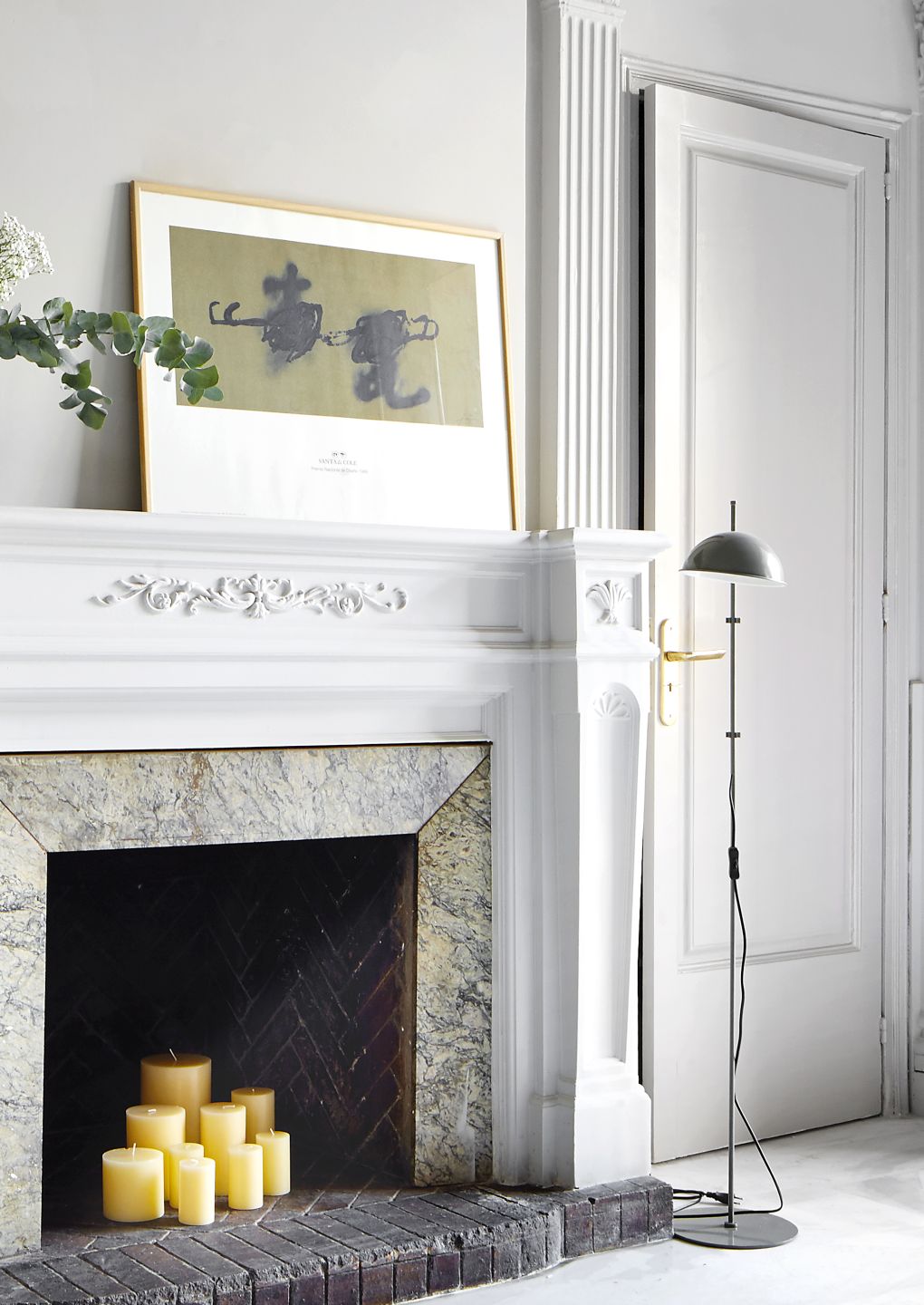 Funiculí Stehleuchte in Perlweiß von Marset neben Kamin mit Kerzen im Wohnzimmer.
