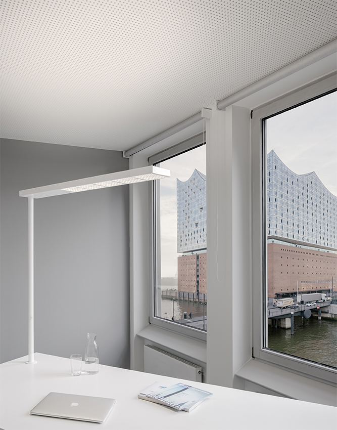 Moderne XT-A Plus Stehleuchte in Grau über einem Schreibtisch mit Laptop und Blick auf die Elbphilharmonie.