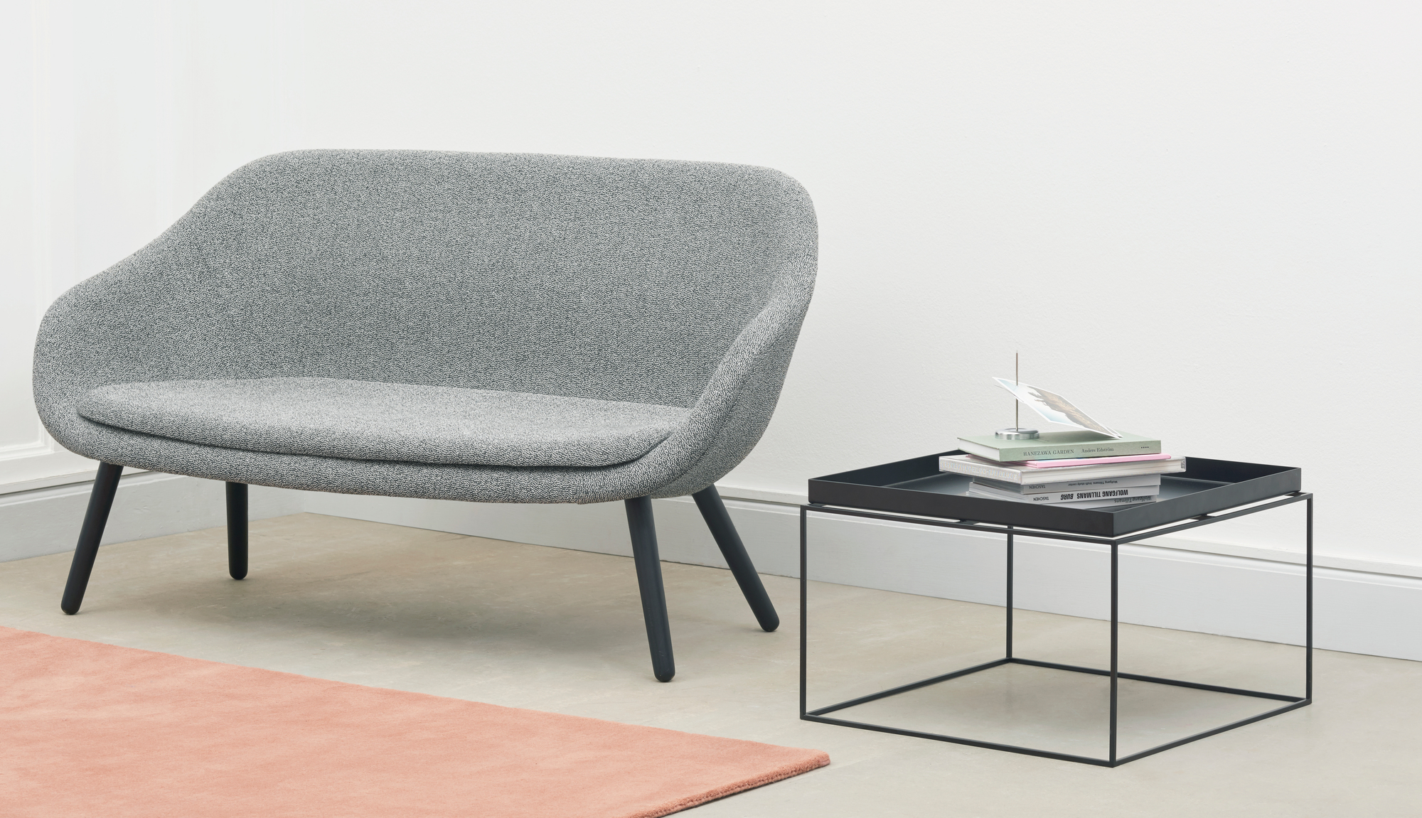 Grauer Sessel neben schwarzem Hay Tray Table Couchtisch mit Büchern und Dekoration in minimalistischem Wohnzimmer.