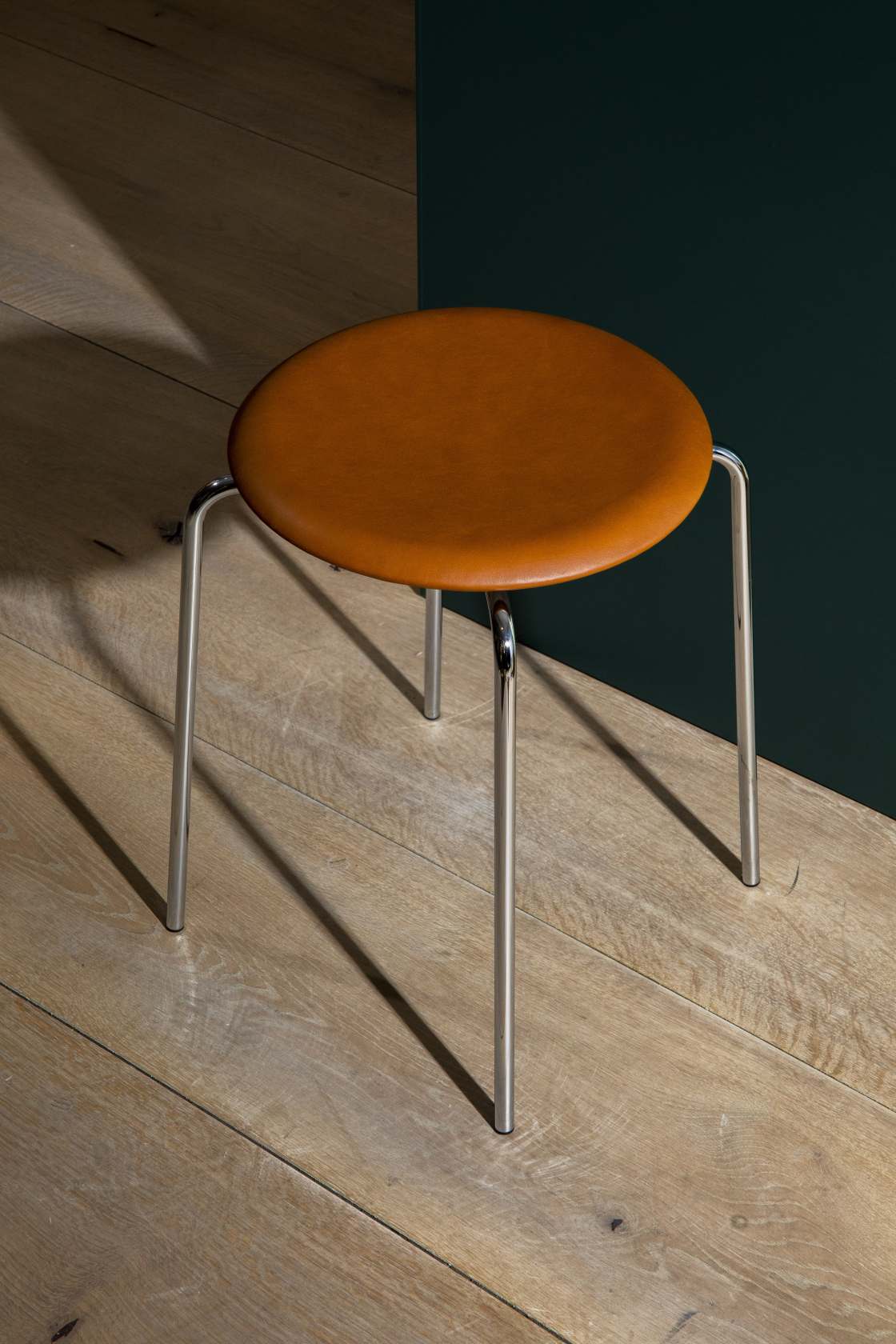Dot Hocker von Fritz Hansen mit braunem Lederbezug und Chromgestell auf Holzboden. Design Hocker.